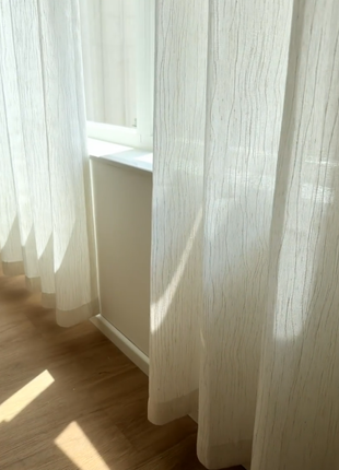 a window with white curtains, allowing sunlight to stream through and illuminate the wooden floor.