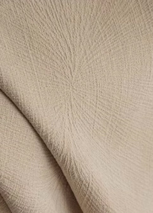 a close-up view of a beige fabric, possibly a blanket or a piece of clothing, with a blurred yellow object in the background.