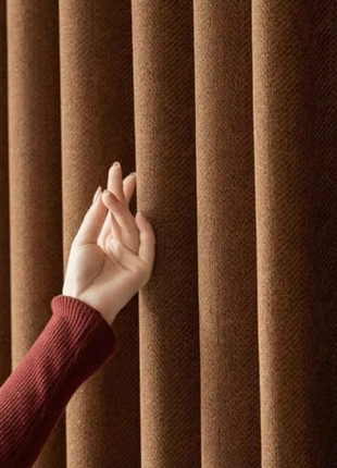 A hand is reaching out to touch a brown curtain, which is hanging from a rod.