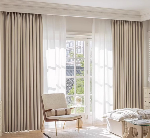 a well-lit living room with a comfortable chair, a glass table, and large windows with sheer curtains.