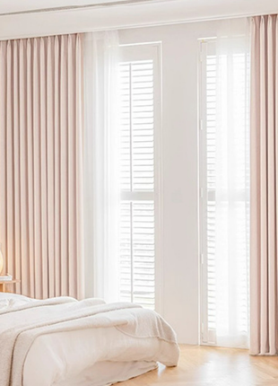 A serene and well-lit bedroom with a bed, curtains, and a lamp on a side table.