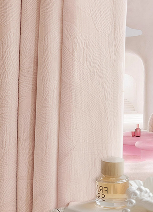 a pink curtain with a white pattern, a bottle of perfume, and a pink table with a white vase on it.