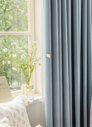 a window with a blue curtain and a white table with a vase of flowers