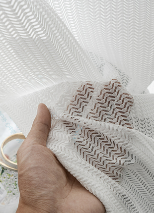 A hand is holding a white fabric with a zigzag pattern, partially covering a magazine or brochure.