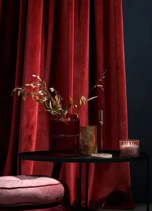 a black table with a pink cushion and a red curtain