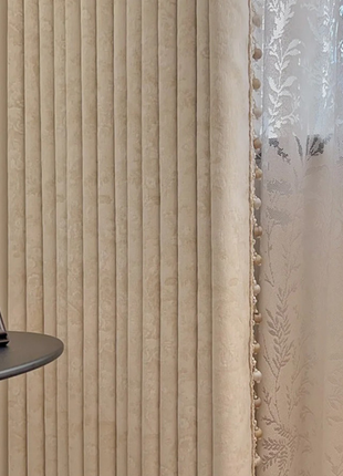 a beige curtain with vertical lines, a framed picture on a shelf, and a window with white lace curtains.