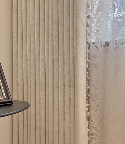 a beige curtain with vertical lines, a framed picture on a shelf, and a window with white lace curtains.