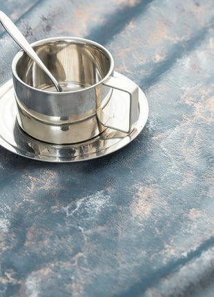 a metal cup and saucer sitting on a table