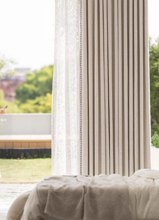 A woman in a white dress stands in a room with a large window, looking at her phone.