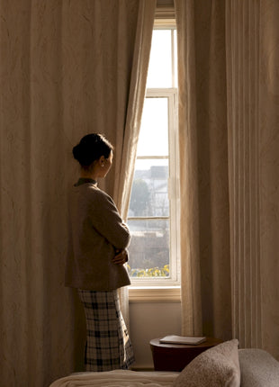 a woman standing in front of a window in a bedroom