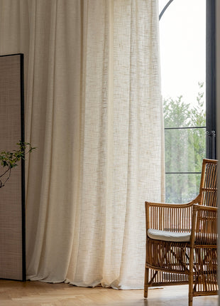 a chair sitting next to a window with a white curtain
