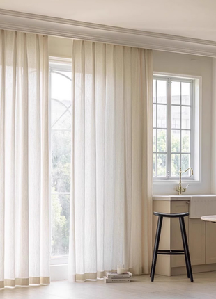 a bright and airy kitchen with a large window, white curtains, and a black stool.