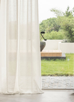 a window with a white curtain and a wooden bench