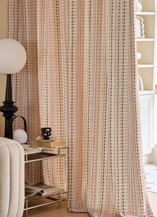 a cozy living room with a white sofa, a black lamp, and a striped curtain. The curtain has a pattern of pink and white stripes, and there are also some books and a small table with a lamp on it.