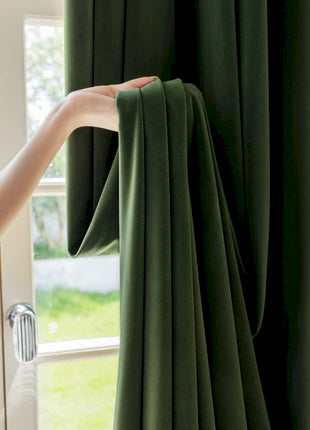 a woman holding a green curtain in front of a window