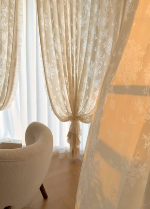 a cozy living room with a plush white sofa and a window adorned with delicate white curtains.