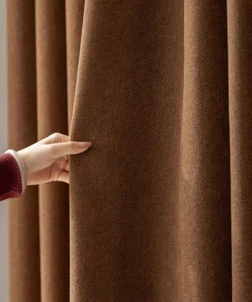 A hand is holding a brown curtain, examining its texture and color.