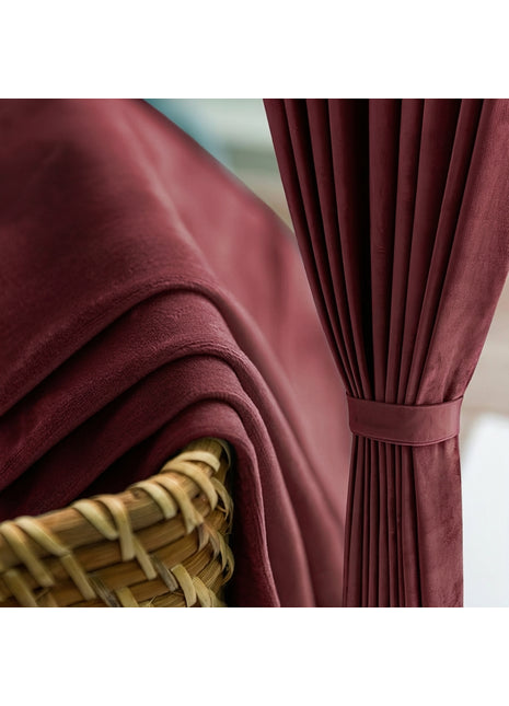 Rideau en velours bordeaux uni retenu par une embrasse assortie, à côté d'un panier en osier