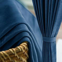 Rideau en velours bleu nuit retenu par une embrasse assortie, plaid en velours sur un panier en rotin