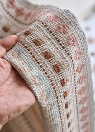 A close-up view of a hand holding a piece of fabric with a patterned design, featuring a mix of pink, gray, and brown colors.