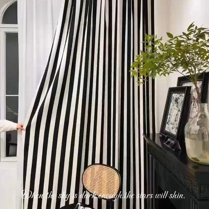 a woman standing in front of a black and white striped curtain