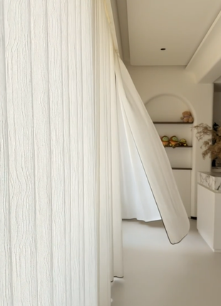 a white room with a white curtain, a white shelf with a vase of flowers, and a white wall with a white shelf.