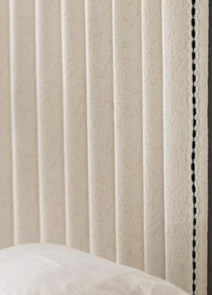 a white wall with a white curtain and a white pillow, along with a branch of purple flowers.