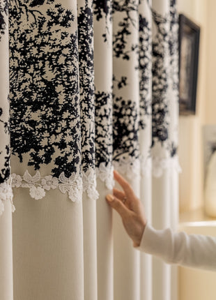 a woman standing next to a window covered in black and white curtains