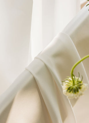 two white flowers sitting on top of a white curtain