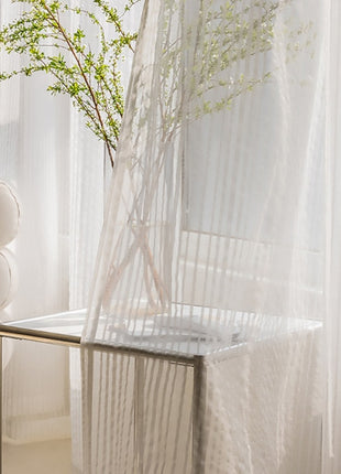 a baby crib next to a window with sheer curtains
