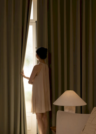 a woman standing in front of a window next to a lamp