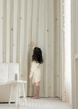 a little girl standing in front of a curtain