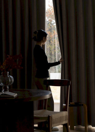 a woman standing in front of a window next to a table