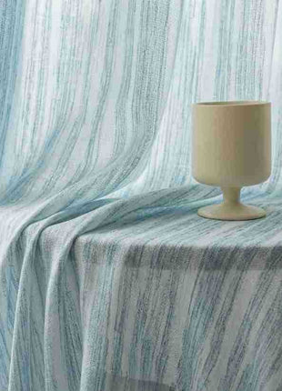 Rideau bleu ciel drapé sur une table avec un verre à pied beige