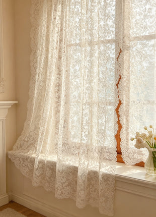 Voilage à broderie florale drapé sur l'appui d'une fenêtre à petits bois