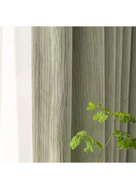 Rideau vert chenille au tissage strié, posé à côté d'un voilage blanc et d'une branche verte